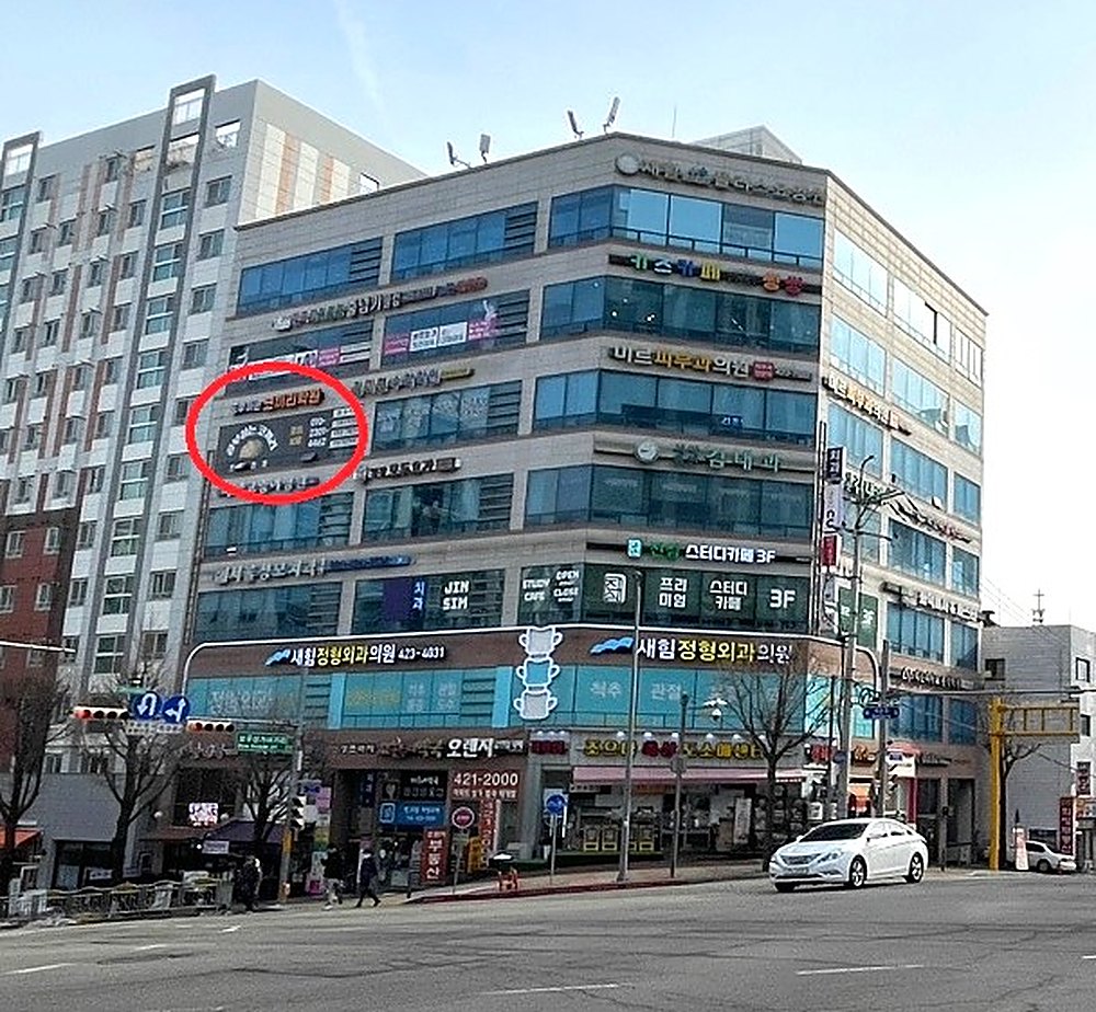 공부하는코끼리수학이 있는 의왕시 내손로 82 신성프라자 건물 외관. 사거리 코너에 있는 건물이며, 5층에 걸린 공부하는코끼리 간판을 빨간 원으로 표시했다. 1층에는 새힘정형외과의원이 있다.